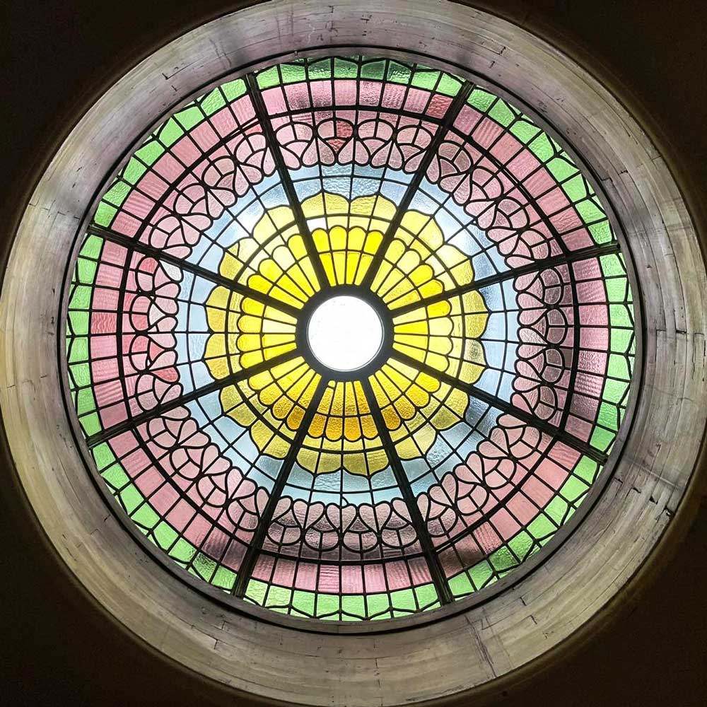 The fully restored leaded stained glass dome at Rookery Hall Hotel photographed from directly below, showing the complete radial design with a central oculus surrounded by concentric bands of yellow, blue, pink and green glass in a scalloped Victorian pattern
