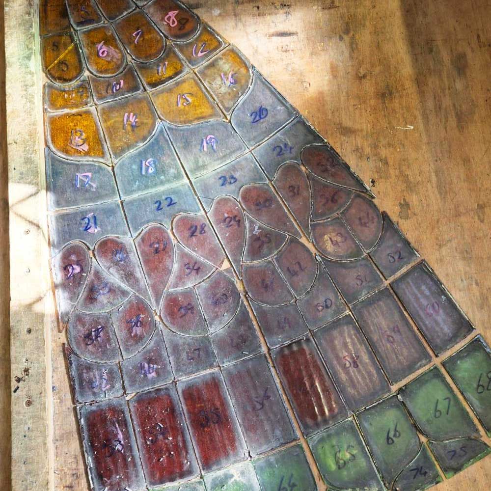 A disassembled dome panel laid flat on a workshop bench, with individual glass pieces numbered for accurate reassembly, showing the full range of amber, mauve, green and burgundy glass types used in the original design