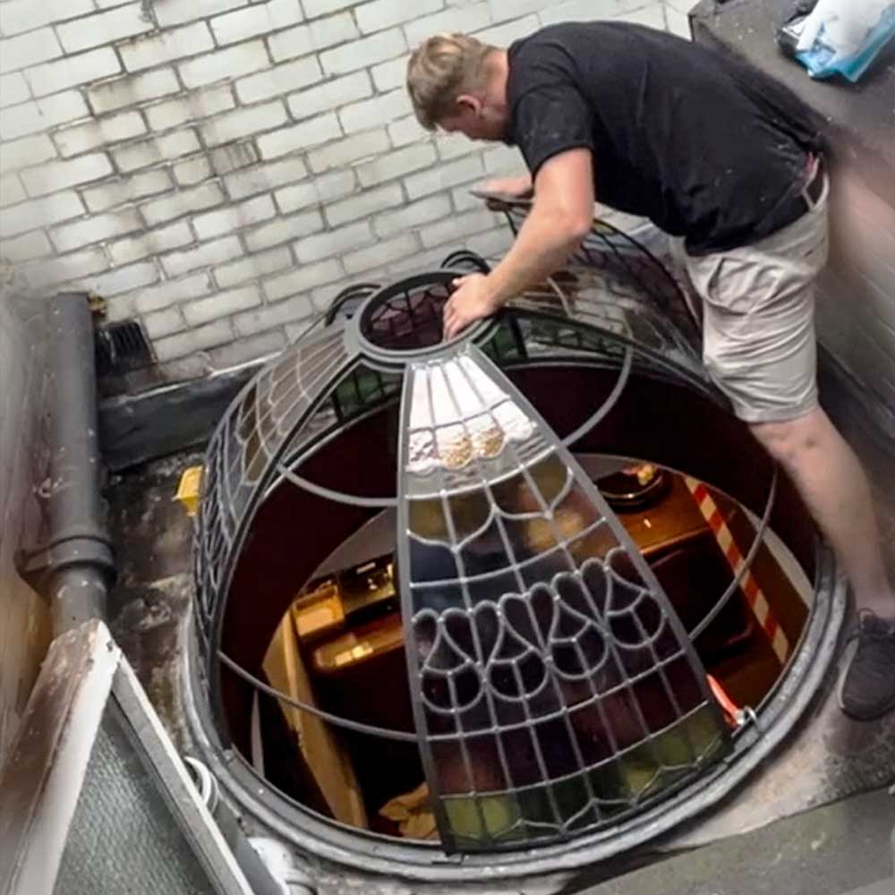 A Hawkscroft craftsman reinstating the restored leaded stained glass dome into its rooftop opening at Rookery Hall Hotel