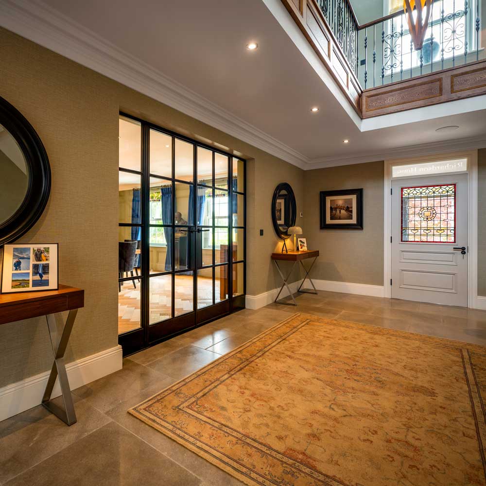 Grand entrance hallway of a house featuring black steel Crittal-style glazed doors, and a traditional stained glass panel in the front door