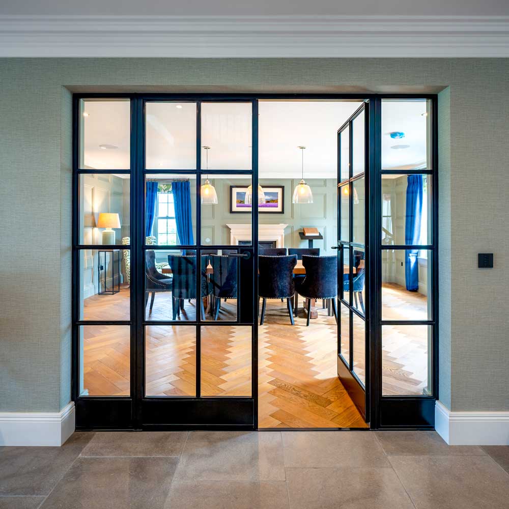 Black steel Crittal-style internal glazed doors standing partially open into a formal dining room